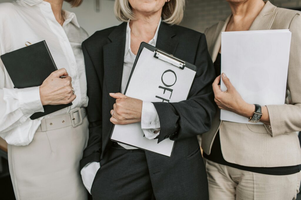 pexels-photo-7433925-7433925 Three businesswomen in attire holding documents and clipboards, conveying professionalism.